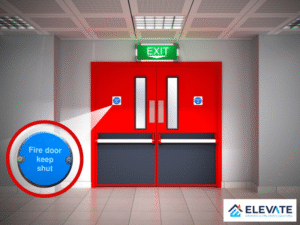 Zoomed-in view of a blue ‘Fire door keep shut’ sign on a red emergency exit door with push bars, located in a commercial hallway. Image includes Elevate Safety Solutions branding.