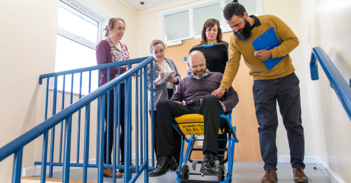Personal Emergency Evacuation Plan (PEEP) in action – staff assisting wheelchair user during fire evacuation.